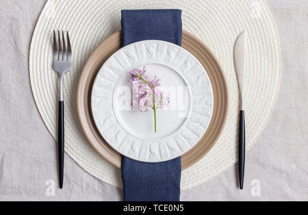 Table set with lilac branch with blue napkin, fork and knife and linen tablecloth. Concept of holiday serving plate Stock Photo