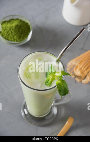 Green cold matcha tea in latte glass with ice cube and milk on grey table. Close up. Stock Photo