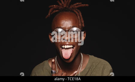 African man with dreadlocks sticking his tongue out looking at camera. Close up of a laughing african male making a funny face isolated on black backg Stock Photo