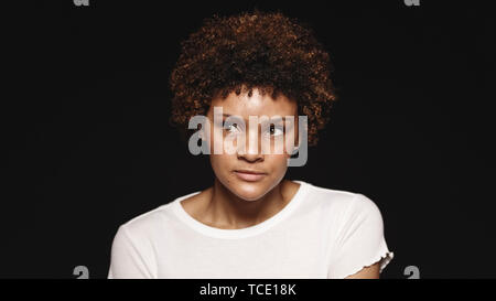 Portrait of a young woman isolated on black background. Close up of a curly haired woman looking away. Stock Photo