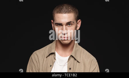 Portrait of a man making faces isolated on black background. Close up of a man looking at camera with a raised eyebrow. Stock Photo