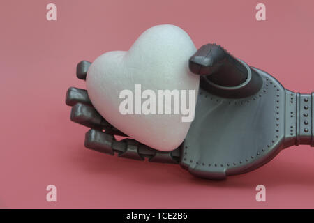 The iron arm of a robot holds a white heart. Concept of robots with a heart. Robots in medicine. Pink background. Stock Photo