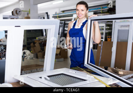 Young american female worker assembling metal-plastic window in workshop, using screwdriver Stock Photo