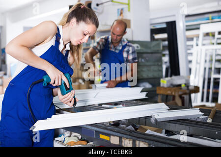 Young female using electric drill on window frame at factory Stock Photo