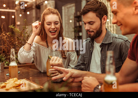 Having fun with friends. Charming long-haired nice-appealing young woman and two happy laughing attractive guys having fun and playing games at the ba Stock Photo