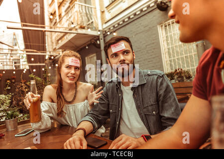 Games at the bar. Confused attractive cheerful good-looking active vigorous mates spending time at the bar playing a hedbanz game Stock Photo