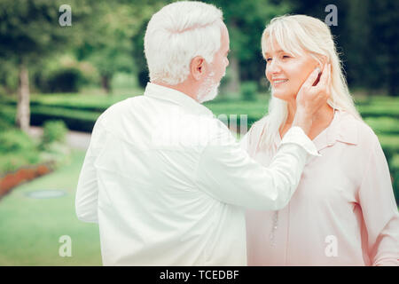 Romantic moments. Delighted nice man touching his wifes cheek while standing with her in the park Stock Photo
