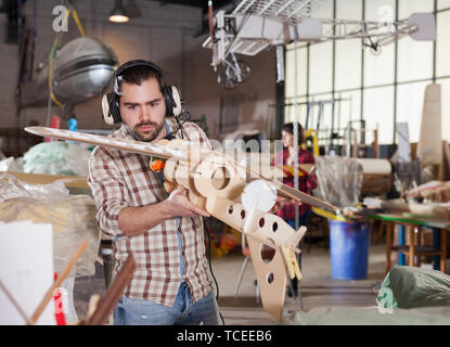 Young handsome bearded man enjoying his hobby - modeling light airplanes in aircraft hangar Stock Photo