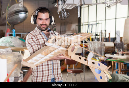 Cheerful male aircraft enthusiast in aviator headphones holding sports airplane models in workshop Stock Photo