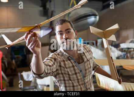Portrait of happy male hobbyist with monoplane models he created in aircraft workshop Stock Photo