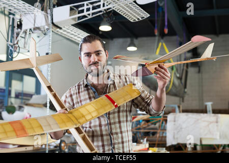 Cheerful male aircraft enthusiast holding sports airplane models in workshop Stock Photo