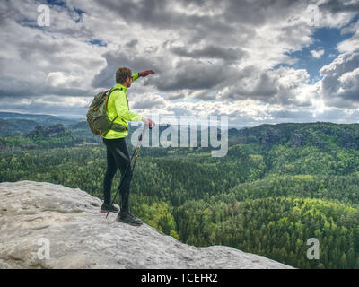 Athlete ginger hair man tourist hiking mountain trail, walking on sandstone rocky hill, wearing backpack and sunglasses, using trekking sticks. Touris Stock Photo