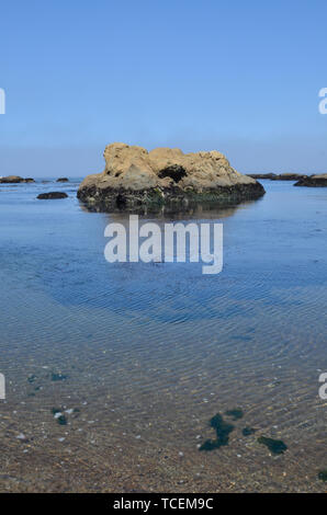 Low tide calm seas reveals a large rock in the ocean Stock Photo