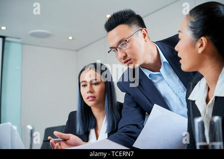Serious Vietnamese entrepreneur discussing important information on computer screen with female colleagues Stock Photo