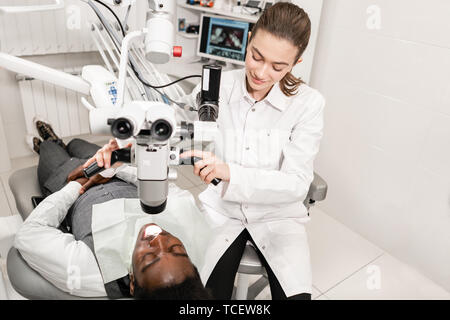 Female dentist advanced user, dental tools. Setup microscope for examining his patients teeth. in dental clinic office. Medicine, dentistry and health Stock Photo