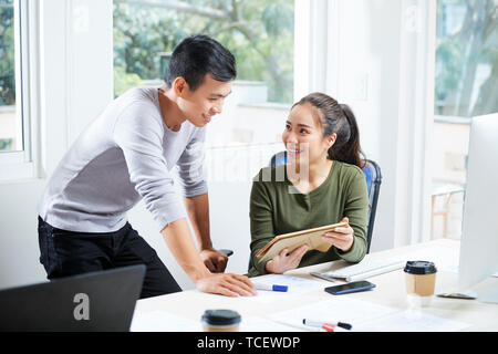 Female UX designer showing her work on tablet computer to smiling coworker Stock Photo