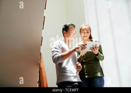 Smiling young Asian man showing tablet computer with his project to female coworker Stock Photo