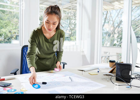 Pensive UI designer choosing icons for new mobile application and putting them on paper wireframe Stock Photo