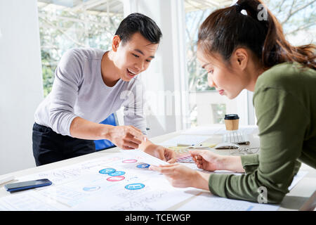 Excited young Vietnamese UI designer showing colleague wireframes and icons he made for new mobile application Stock Photo