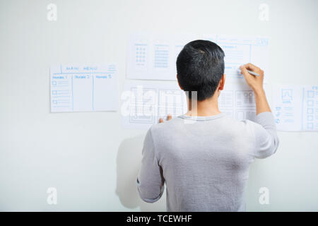 Rear view of professional UI designer drawing wireframes for project on office wall Stock Photo