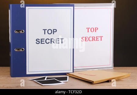 Envelopes and folders with top secret stamp and photo papers on wooden table on brown background Stock Photo