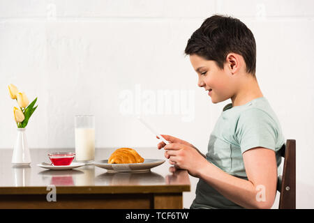 side view of smiling boy using digital tablet during breakfast in kitchen Stock Photo