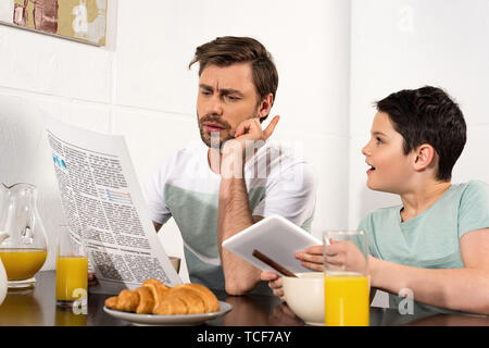 focused father reading newspaper and son using digital tablet during breakfast Stock Photo