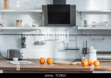 modern kitchen with juicer, glass and tasty organic oranges on wooden table Stock Photo
