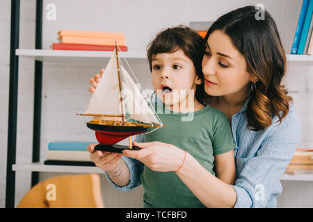 Mother and surprised kid with toy ship in living room Stock Photo