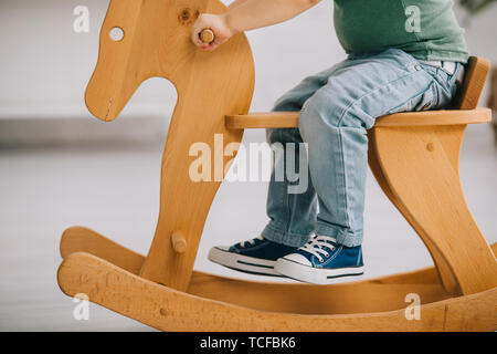 cropped view of child sitting on wooden rocking horse in living room Stock Photo