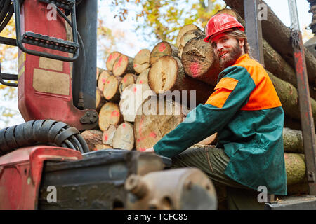 Young forest worker as crane operator at the wood harvest boards the forwarder Stock Photo