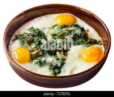 Traditional Catalan fried eggs with spinach, raisins and ham served in clay bowl. Isolated over white background Stock Photo
