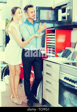 Young man and woman are choosing new microwave in kitchen furnishing store. Stock Photo