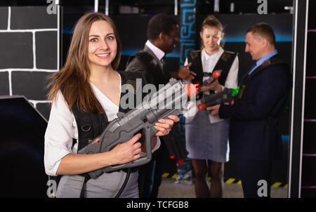 Woman in business suit holding her laser gun and playing laser tag with colleagues Stock Photo