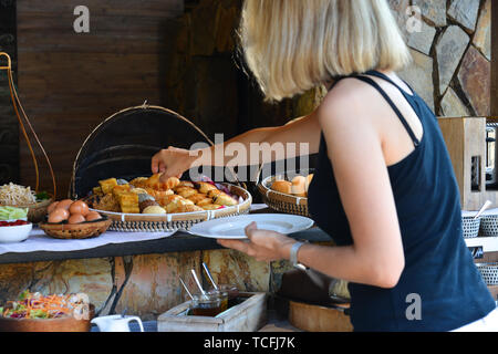 Self service took the food from the buffet line. A young woman taking food for breakfast. Stock Photo