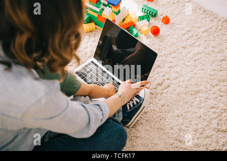 Cropped view of mother and son sitting on carpet and using laptop Stock Photo