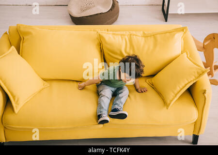 Little boy in green t-shirt sitting on yellow sofa Stock Photo