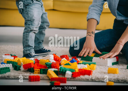 cropped view of mother and son playing with lego on carpet in living room Stock Photo