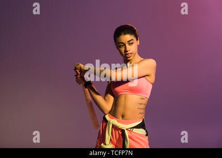 pretty african american girl in pink sports bra holding baseball bat on purple background Stock Photo