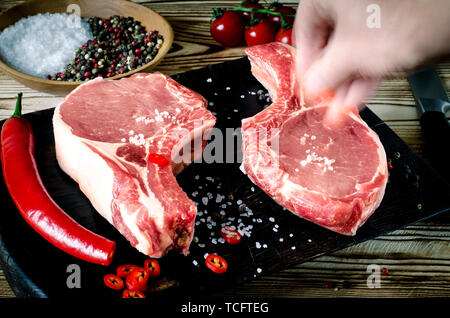 hand salt meat steak. Raw marbled meat steak, pepper, herbs, garlic, old wooden background. Space for text. Beef Rib eye steak ready for cooking. Stock Photo
