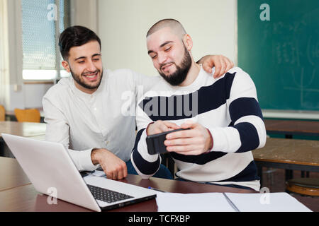 Two young students distracting from their studies and watching at gadget Stock Photo
