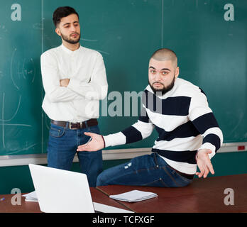 Quarrel between two young male students in classroom Stock Photo