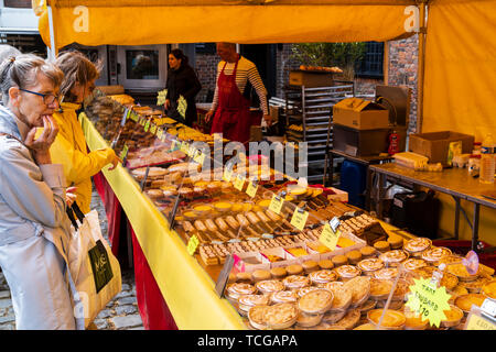 Le Weekend event French market at Sandwich, England. Two mature women looking and thinking about which cakes to buy from French bakery stall. Counter covered in various French cakes and tarts. Stock Photo