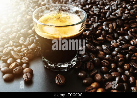 glass filled with dark  hot espresso coffee and roasted coffee beans on table Stock Photo