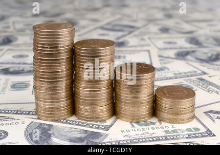 Stack of ukrainian coins in stacks falling down. Ukrainian money lies on US hundred dollar bills Stock Photo