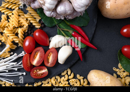 top view of fresh ingredients. Healthy cooking background with organic vegetables and pastas for vegan on black slate . tomato , garlic and fresh chil Stock Photo