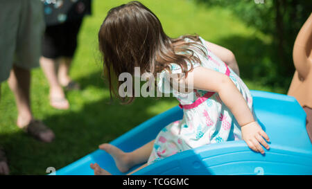 Multi-ethnic child having fun going down small slide with family and friends in the background Stock Photo