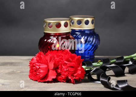 Memory lantern with candles, red carnations and ribbon on wooden table on grey background Stock Photo
