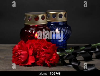 Memory lantern with candles, red carnations and ribbon on wooden table on grey background Stock Photo