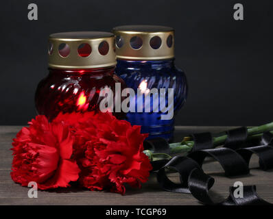 Memory lantern with candles, red carnations and ribbon on wooden table on grey background Stock Photo